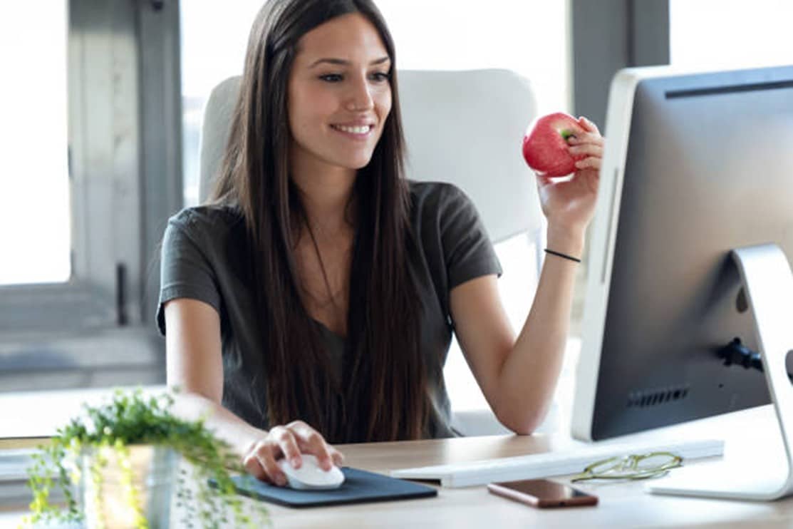 mujer delante ordenador comiendo una manzana